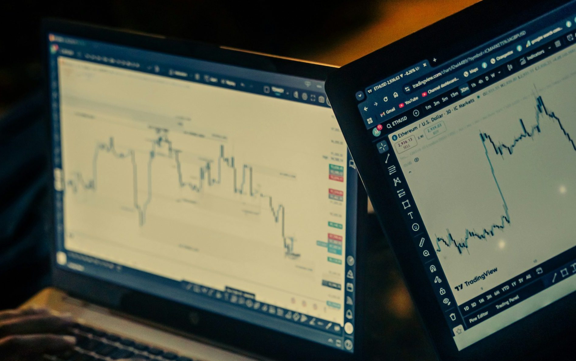 Hands typing on laptops with stock charts displayed.